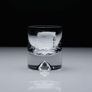 Clear glass with a large ice cube on a reflective surface with a black background
