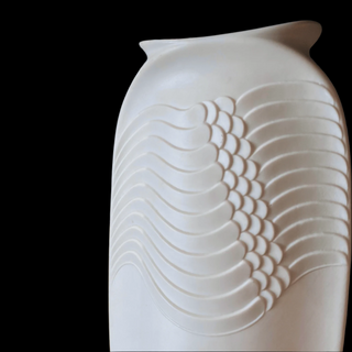 White ceramic vase with wavy design next to a yellow square plate on a dark surface.