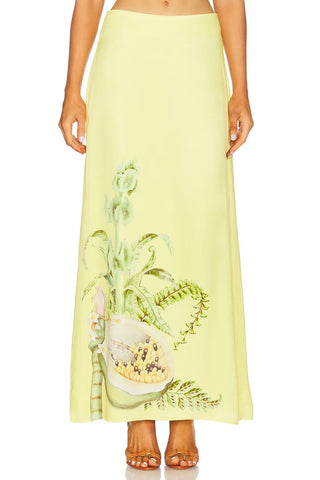 A model wearing a pale yellow-green maxi skirt with a botanical print of a potted plant and a guava, shown against a plain white background.