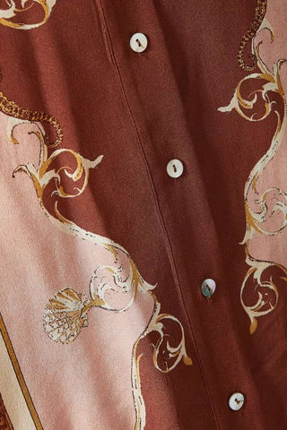 Close-up of a button-front garment in a dusty rose-brown fabric with a contrasting pale pink panel and ornate gold scrollwork print.