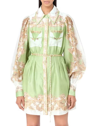 A model wearing a light green mini shirt dress with white panels and beige floral embroidery, featuring a pointed collar, long sheer sleeves, and a matching waist tie.