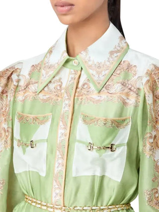 A close-up of a model wearing a light green and white silk shirt with ornate gold baroque patterns, featuring two front pockets with gold horsebit details.