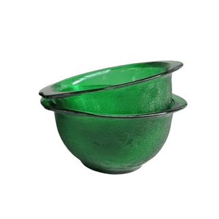 Two green glass bowls stacked on a white surface with a light pink background