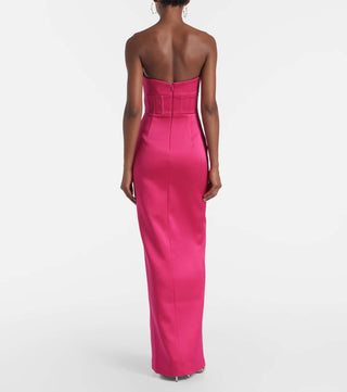 A woman shown from the back wearing a strapless, floor-length magenta pink gown with structured detailing at the waist, photographed against a clean white studio background.