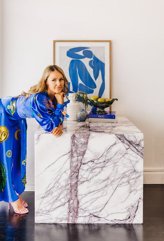 Model wearing Alemais Soleil Hire Dress leaning on table with various secondhand homewares and artwork