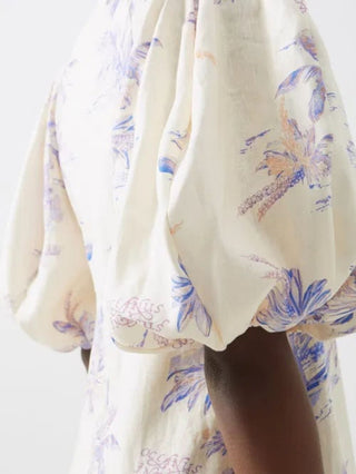 Close-up of a cream-coloured dress with a blue and purple floral print, featuring voluminous puff sleeves and gathered fabric.
